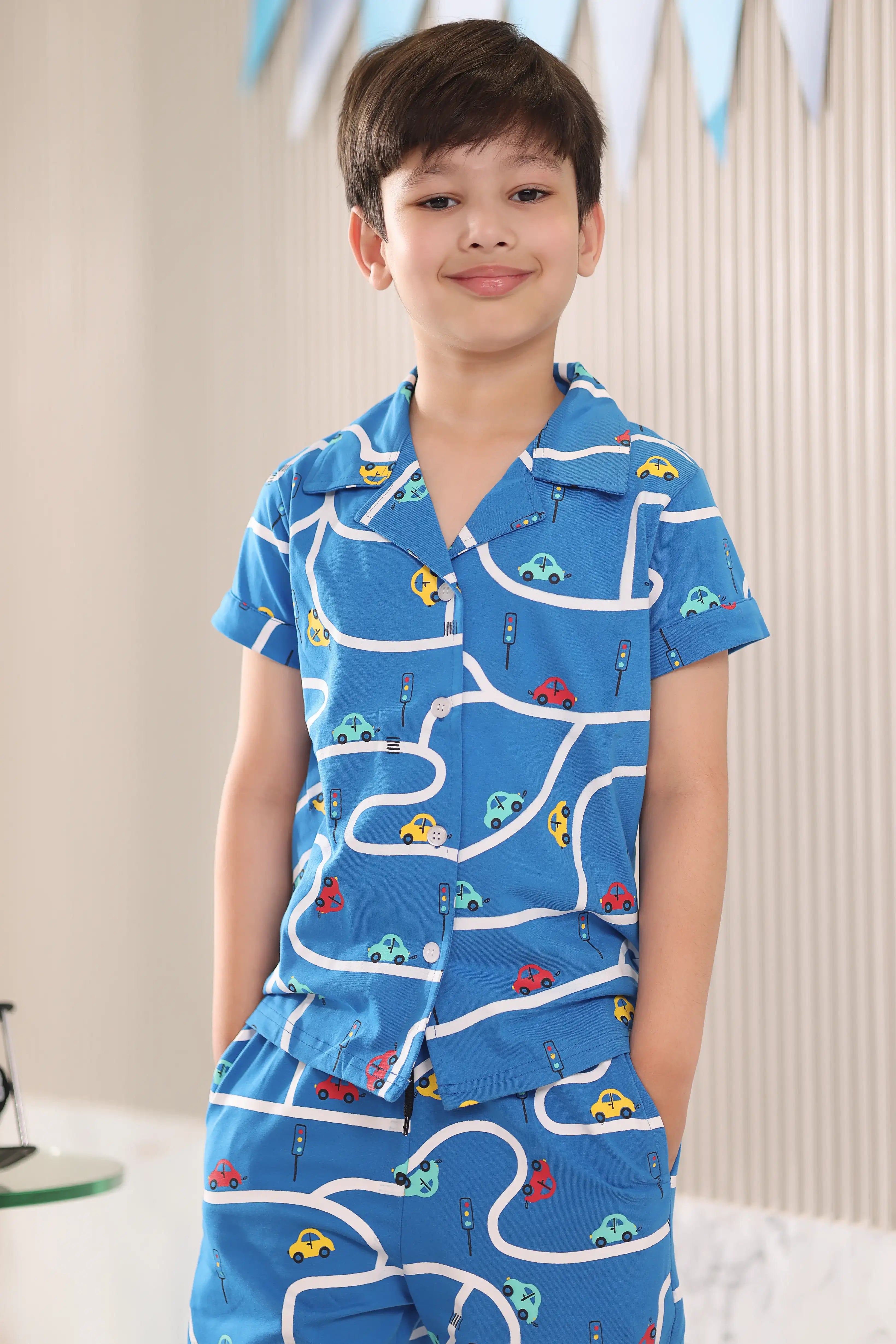Kid wearing a blue pajama set with car patterns against a neutral background