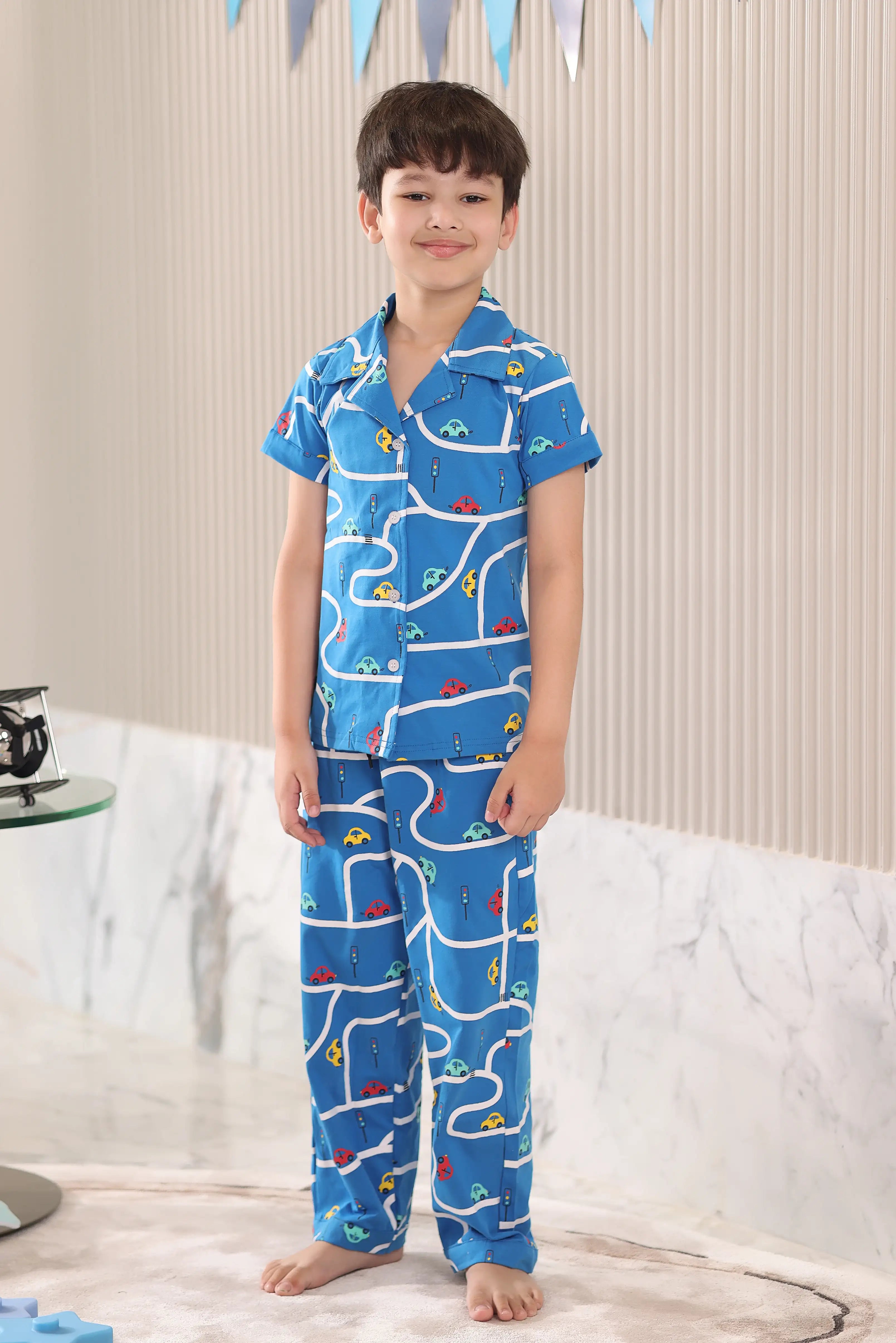 Child wearing a blue pajama set with a car pattern standing on a neutral background