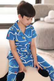 Child wearing a blue pajama set with car patterns sitting on a couch.