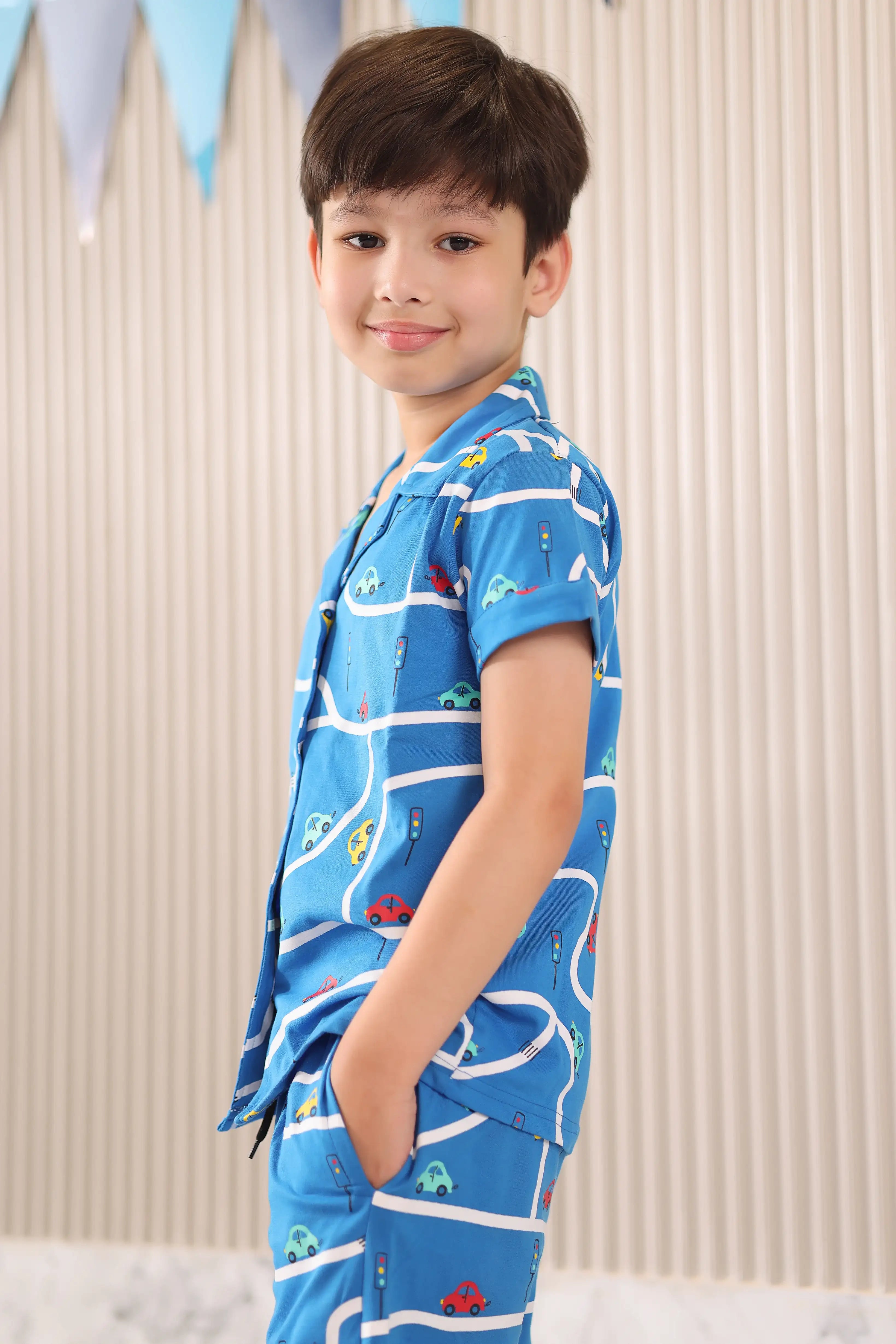 A boy wearing a blue shirt with car patterns against a neutral background