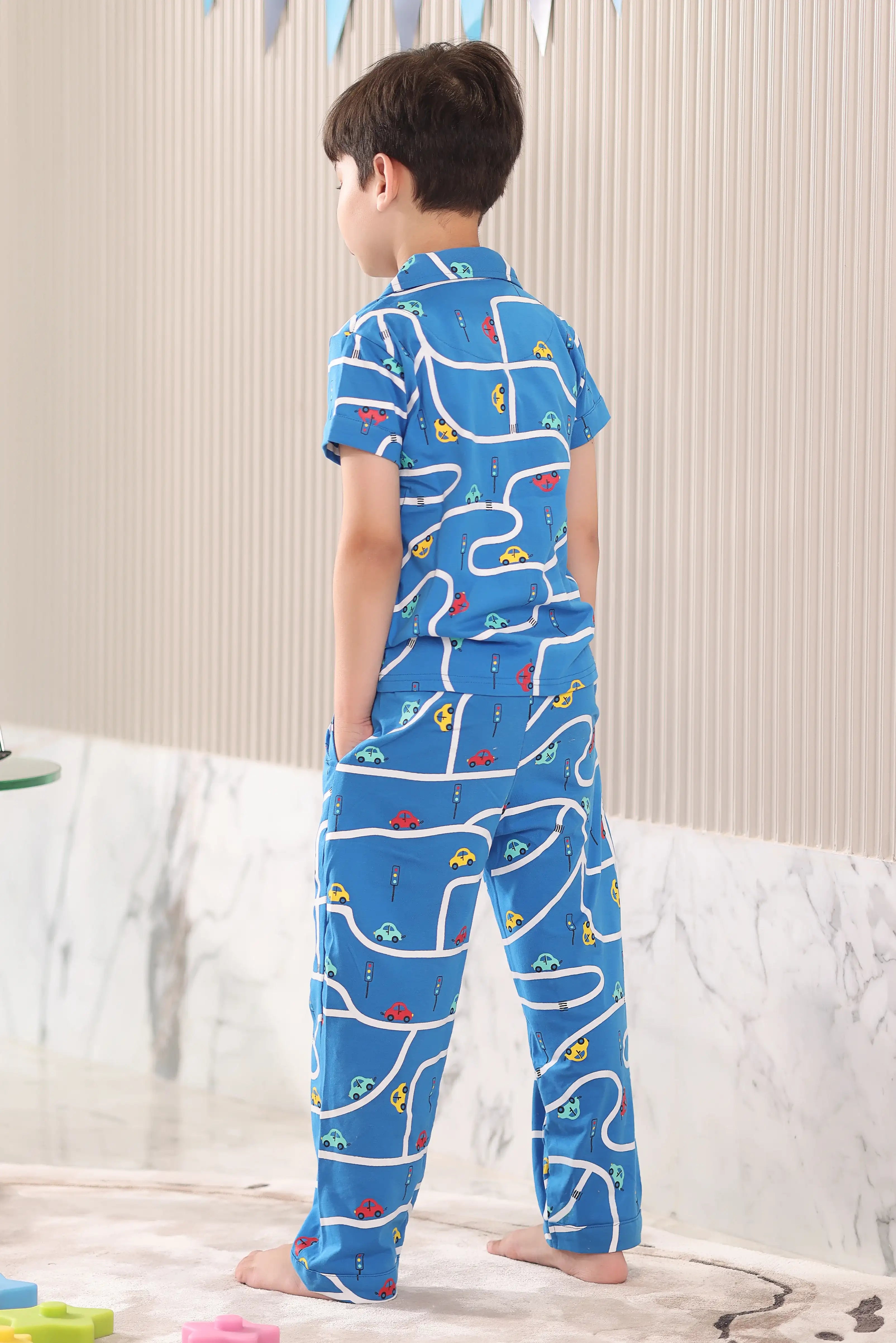 A child wearing a blue pajama set with a car pattern, standing in a back view pose in a room.