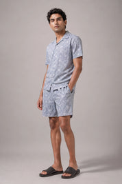 Man wearing a light blue patterned shirt and shorts on a gray background