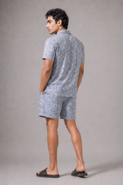 Man wearing a gray patterned shirt and shorts set against a plain background
