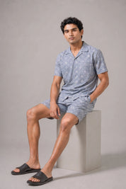 Man wearing a light blue pajama set sitting on a white block against a gray background