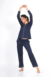 Young woman in a solid navy 100% cotton full sleeve nightsuit by NapStory, stretching her arms overhead with a joyful smile.