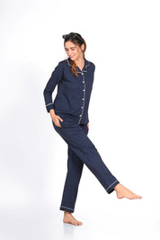Smiling young woman in a solid navy full sleeve 100% cotton nightsuit by NapStory, playfully lifting one leg while standing.
