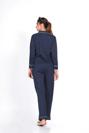 Woman in a solid navy full-sleeve 100% cotton nightsuit by NapStory, standing with her back to the camera, displaying the comfortable and breathable fabric of the nightwear.