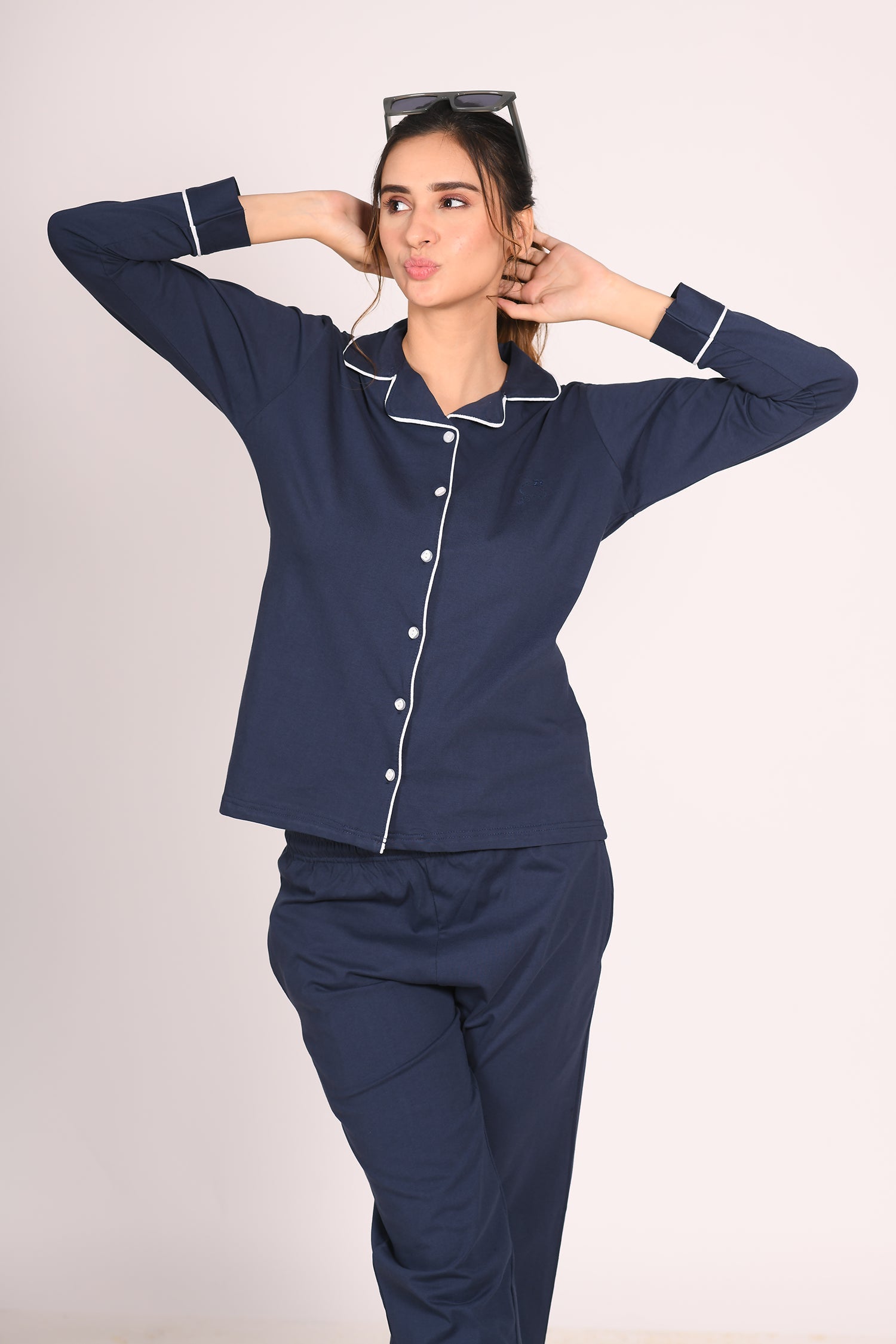 Woman wearing a solid navy 100% cotton full sleeve nightsuit by NapStory, posing playfully with her hands behind her head and a relaxed expression.