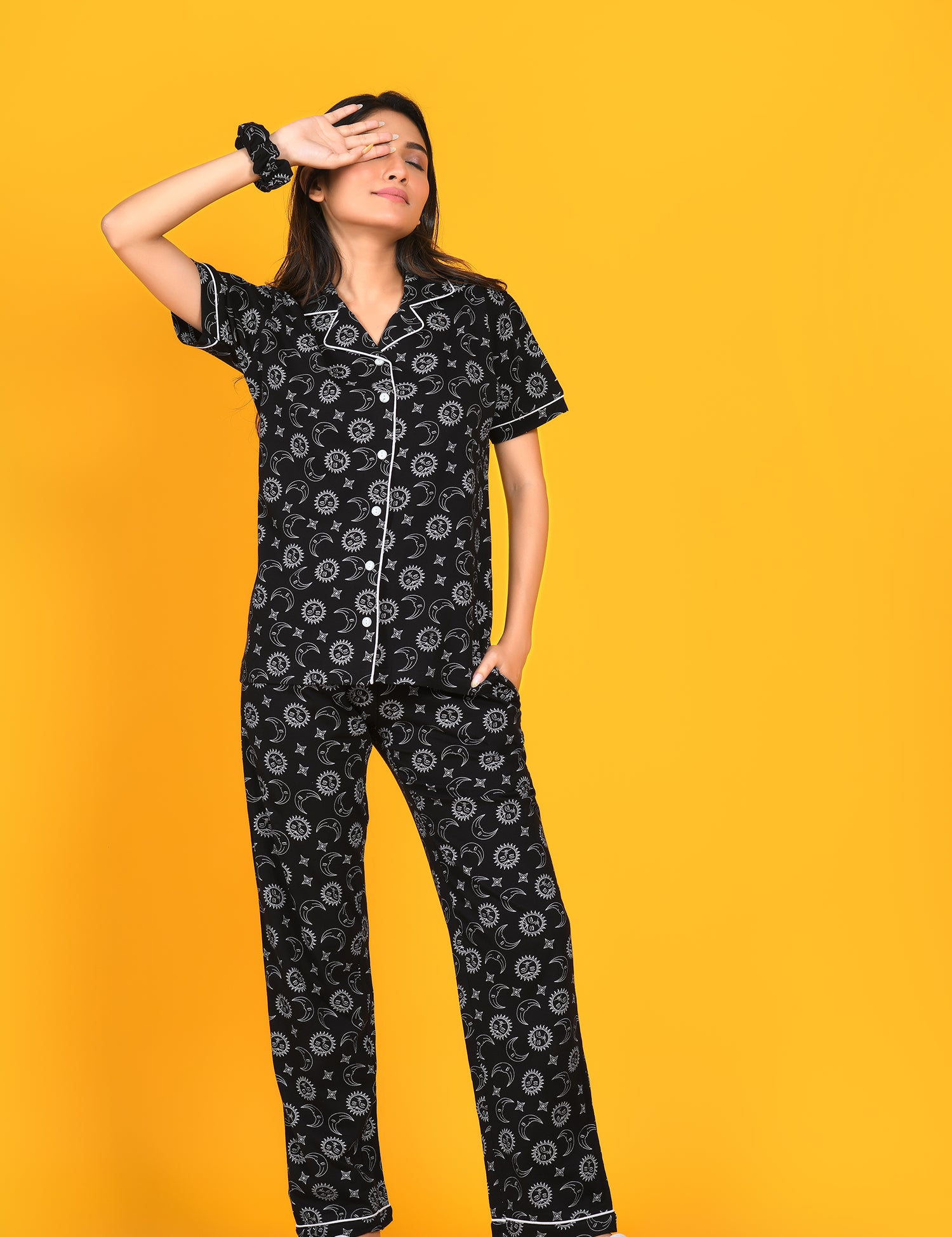 A girl wearing a black Star Moon Print Pyjama Set nightwear by NapStory, gently resting one hand on her eye and the other hand tucked away.