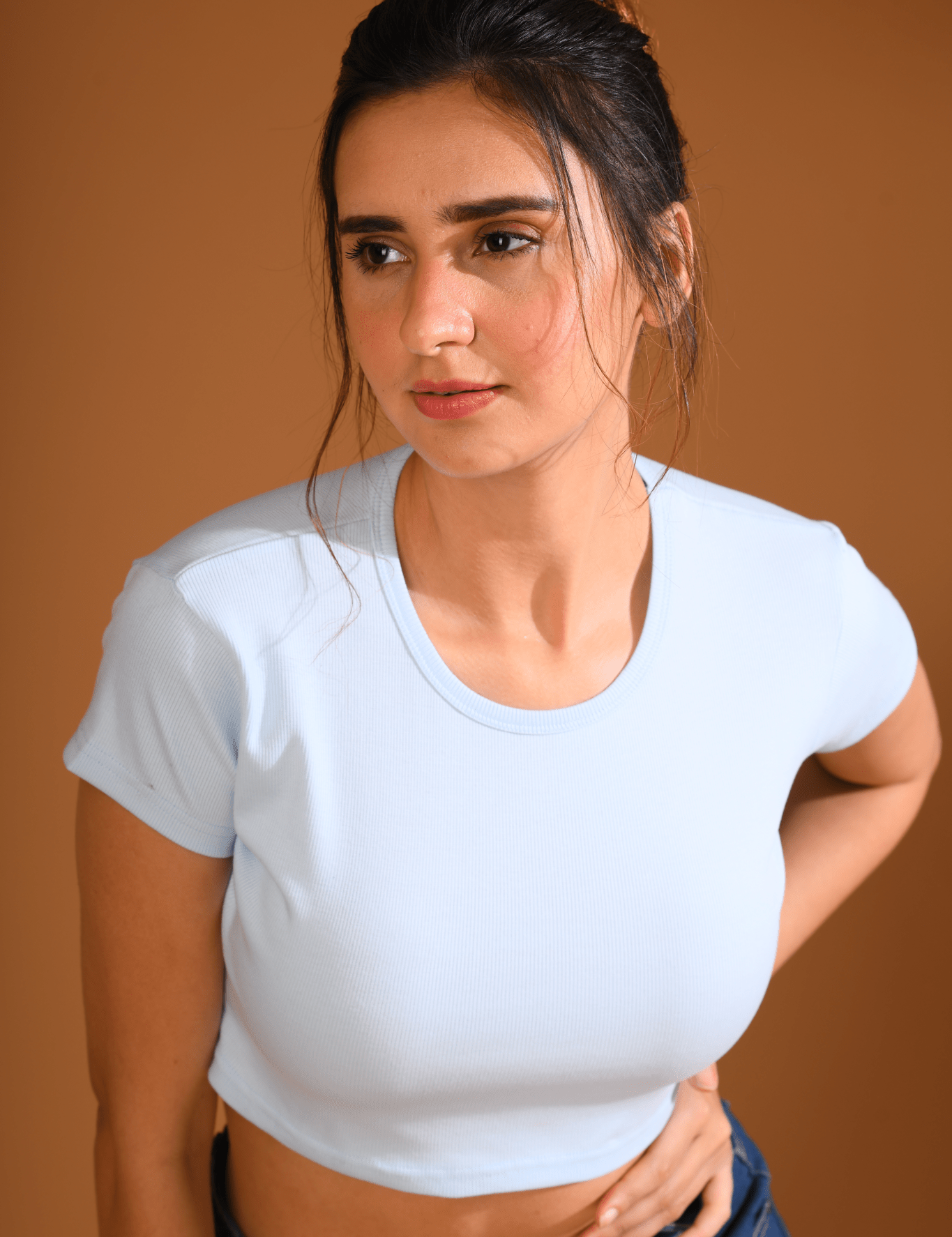 A young girl wearing a Sky Blue Baby Tee by NapStory, leaning forward in a confident pose.